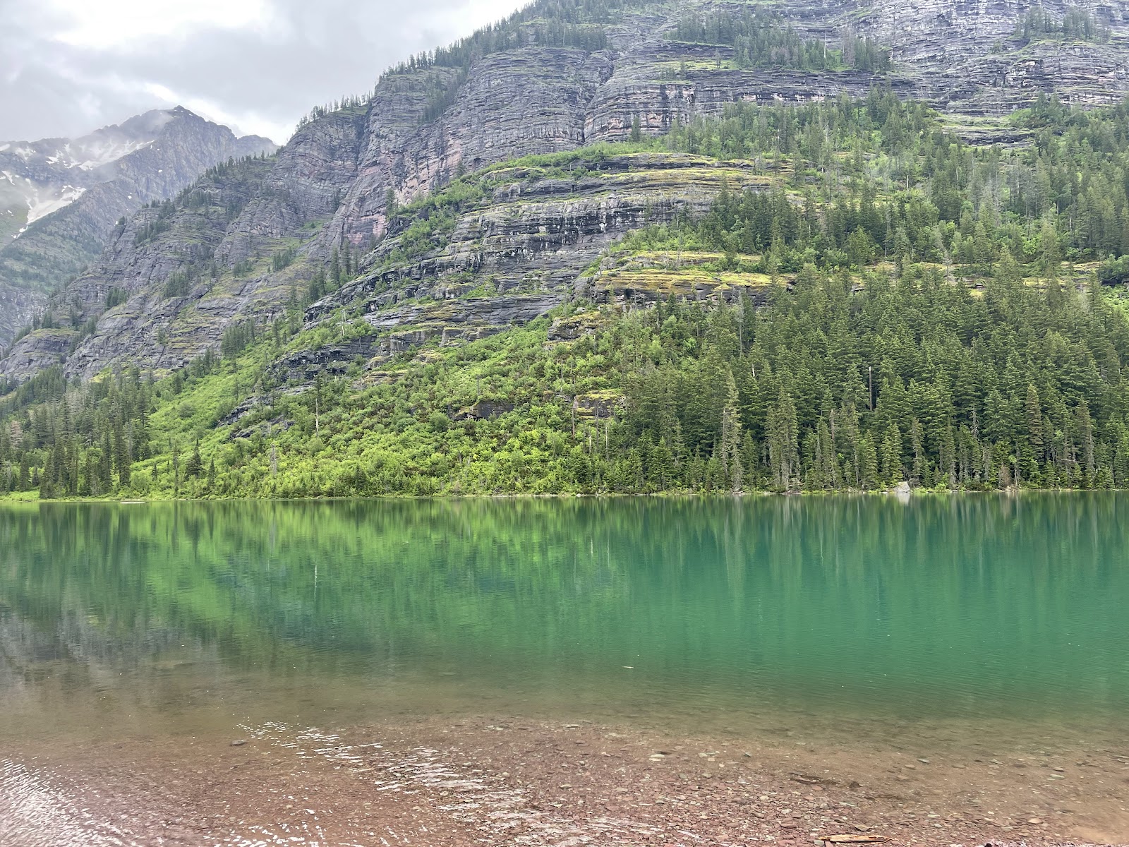 Avalanche Lake Trailhead at Glacier National Park, turquoise lake reflecting forested cliffs and rugged mountains.