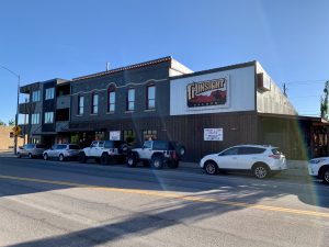 Saloon exterior on a main street in Glacier National Park, a two-story brick building with red-trimmed windows and parked cars along the curb.