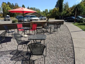 Outdoor patio seating with metal tables and a red umbrella at a Glacier National Park-area brewery near the parking lot.