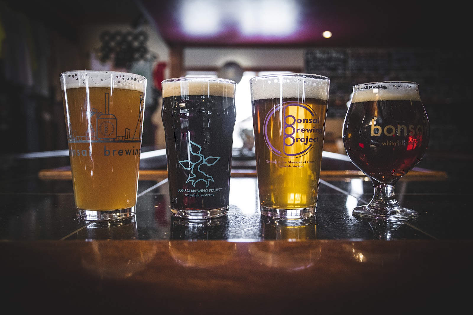 Four craft beers lined up on a glossy bar at a Glacier National Park‑area brewery in Montana.