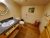 Rustic cabin bathroom with gray countertop and white sink, oval mirror, toilet, wooden open shelves of toilet paper, red stool, and a wall photo in Glacier National Park.