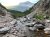 Apikuni Falls area along a rocky stream in Glacier National Park, Montana, with rugged talus and distant forested slopes.