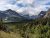 Apikuni Falls overlook at Glacier National Park, with snow-dusted peaks, lush forest, and a turquoise lake in a dramatic valley.