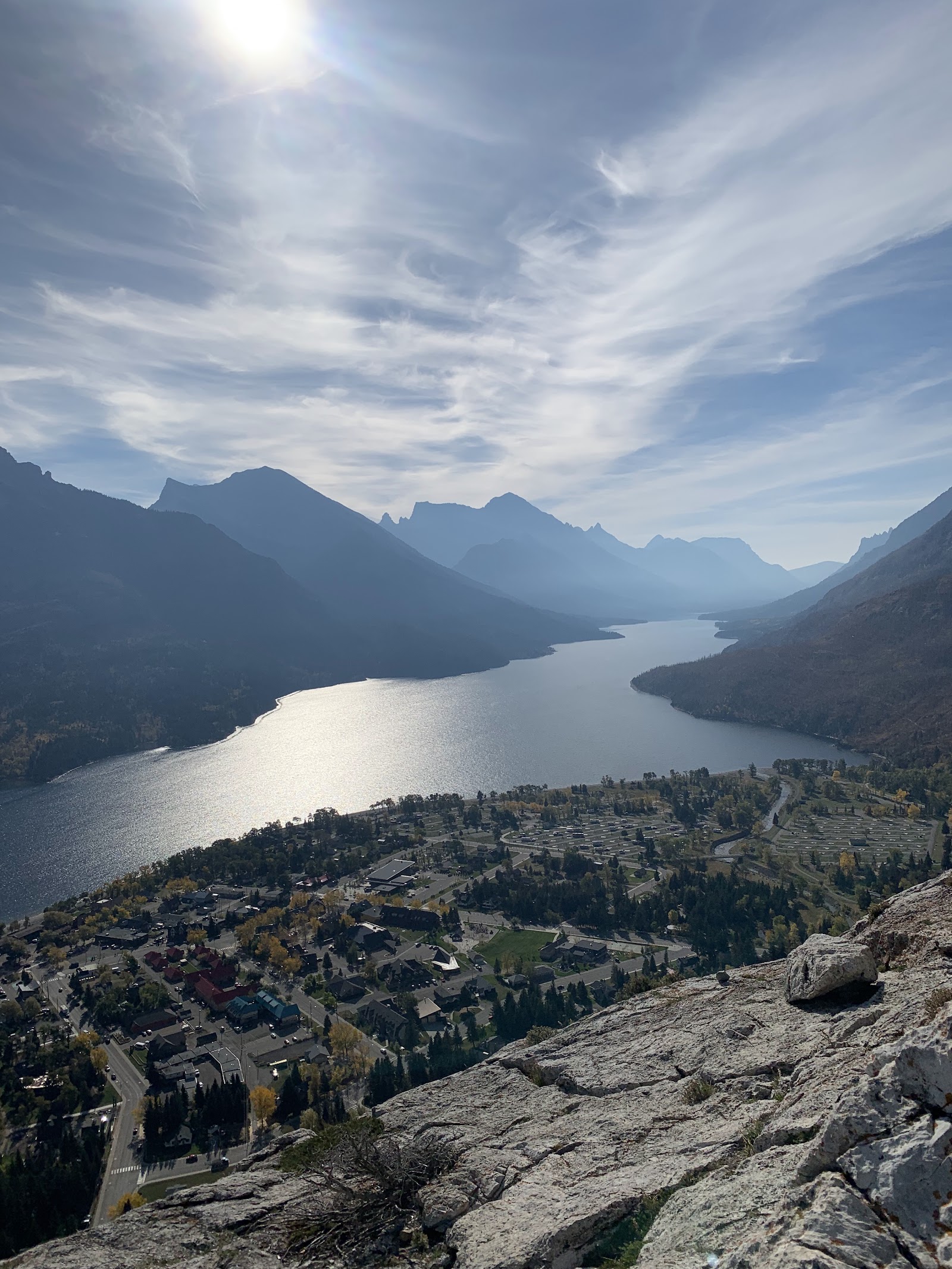 Bertha Trailhead overlook in Glacier National Park frames a winding lake with jagged mountains and a bright sky.