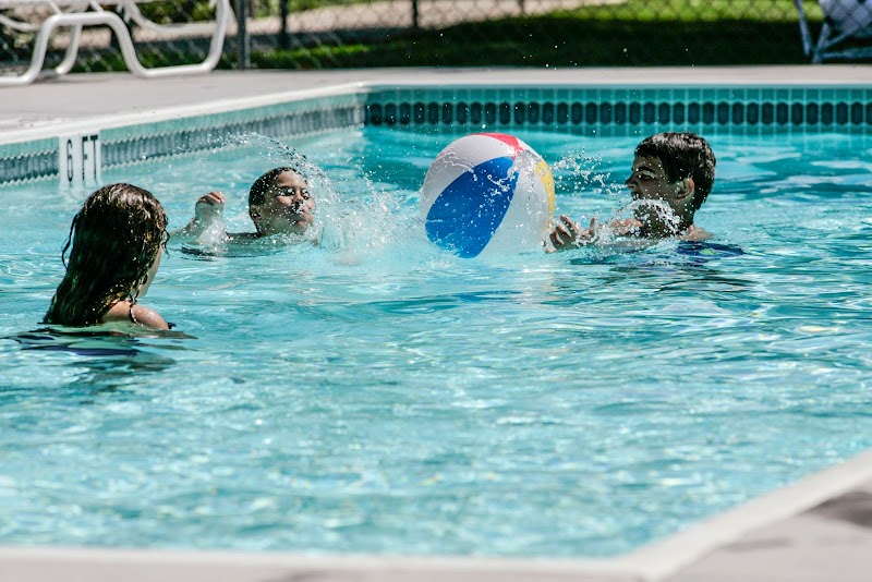 Three kids splash in a pool, chasing a multicolor beach ball in Yellowstone National Park.