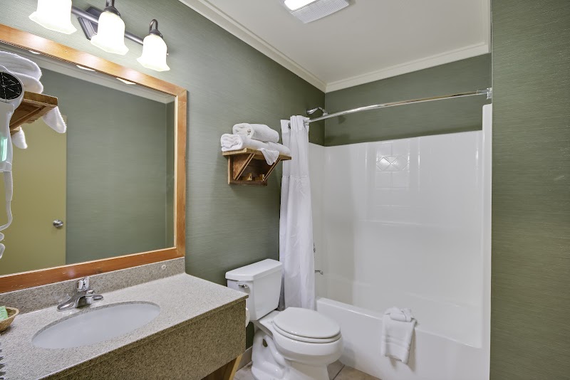Green-walled Yellowstone National Park lodge bathroom with granite counter, mirror, toilet, towels, and white tub/shower.
