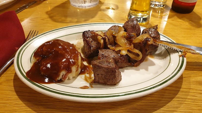 Plate of steak chunks with sautéed onions and mashed potatoes with gravy on a wooden table in Yellowstone National Park.