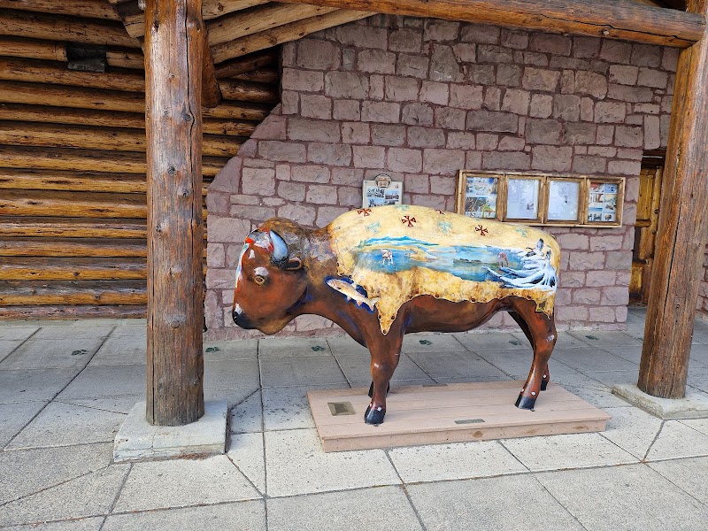 Brown cow statue with a painted saddle blanket stands on platform beside a stone wall at Yellowstone National Park.