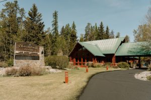 Rustic log cabin lodging at a Glacier National Park resort, with a green-roofed lodge and forest backdrop.