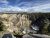 Lookout Point, Yellowstone National Park: rugged canyon walls, a winding river, evergreen trees, and a rainbow over patches of snow.