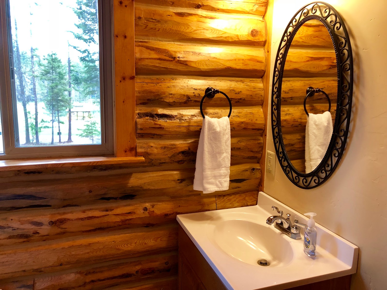 Rustic log cabin bathroom with an ornate oval mirror, towel ring, and sink in Glacier National Park.