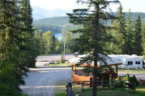 Forest campground in Glacier National Park with a wooden gazebo, gravel road, and parked RVs against distant mountains.