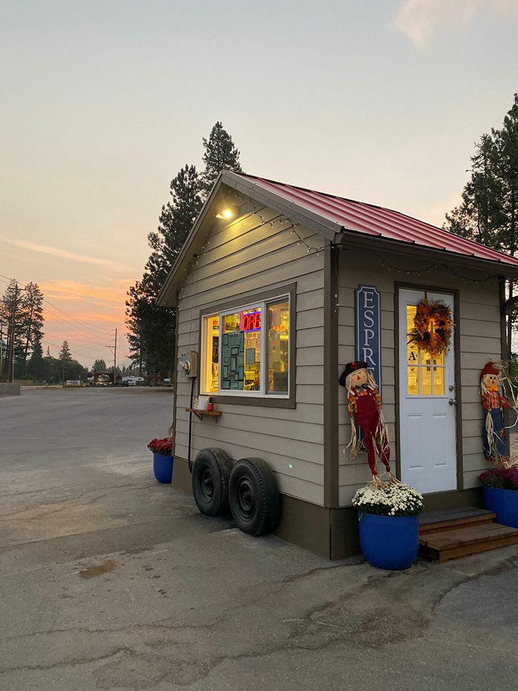 Small roadside espresso stand in Glacier National Park, decorated with autumn wreaths and string lights at dusk.