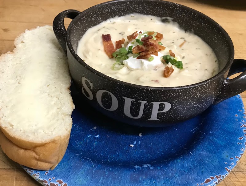 Creamy soup in a speckled black pot labeled SOUP sits on a blue plate with bread beside it in Yellowstone National Park.