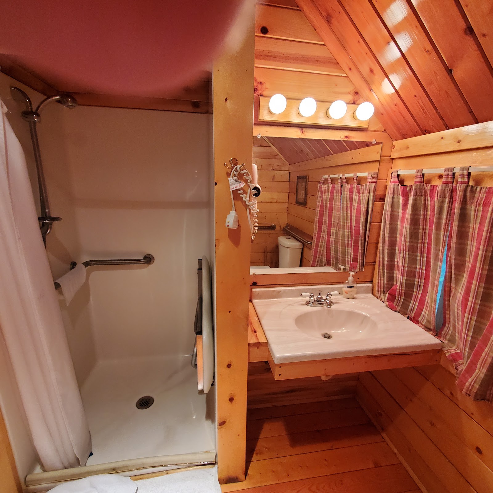 Cozy wooden bathroom in a cabin at Glacier National Park campground, featuring a shower, sink, mirror, and plaid curtains.