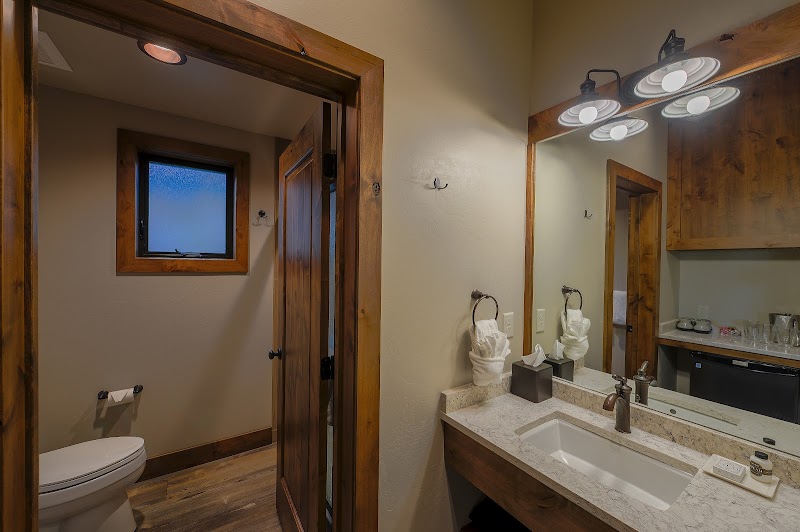 Bathroom with double vanity, granite countertop, dark wood cabinets, large mirror, towels, and a separate toilet room in Yellowstone National Park.