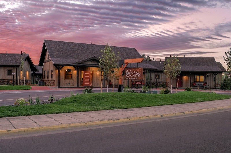 Rustic wood lodge complex with warm lights and a manicured lawn under a pink sunset in Yellowstone National Park.
