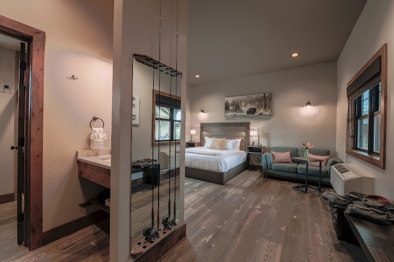 Spacious hotel suite with a king bed, a blue sofa, coffee table, wall art, and a light-filled window in Yellowstone National Park.