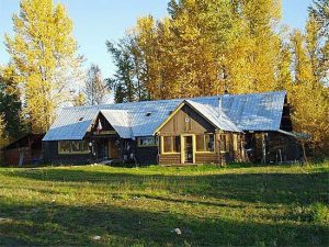 Front view of a rustic hostel in Glacier National Park, surrounded by golden fall aspen trees and a metal roof.