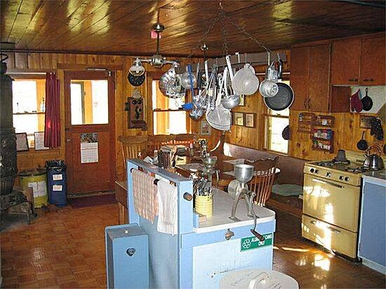 Interior of a rustic Glacier National Park hostel kitchen, with pots and pans hanging above a blue island.
