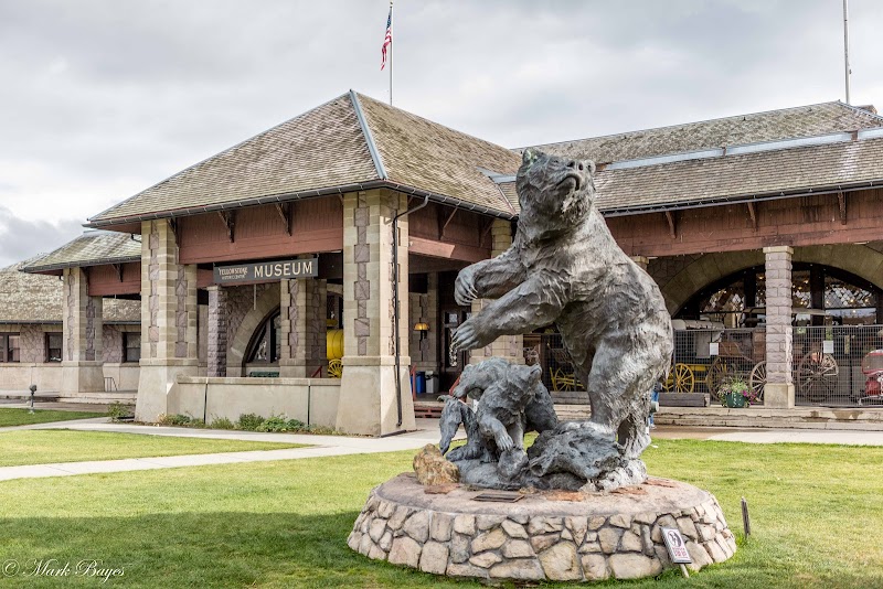 Yellowstone National Park visitor center with stone columns and a large bear statue on a pedestal in front of a building