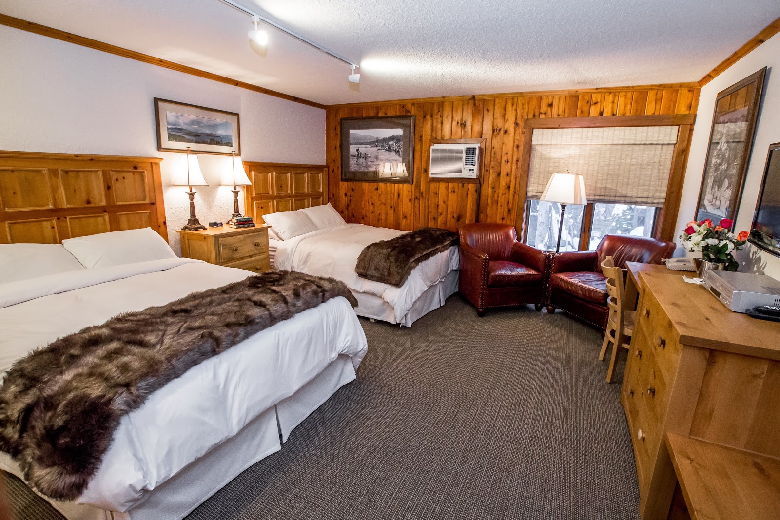 Two-queen bed lodge room with fur throws and wood paneling, Glacier National Park area.
