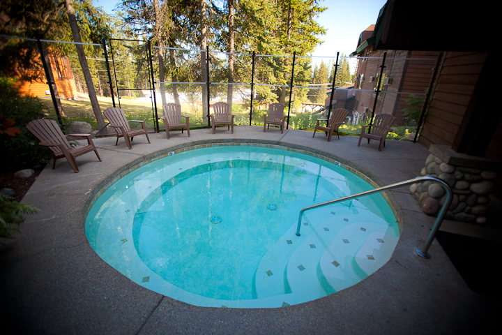 Kandahar Lodge pool at Whitefish Mountain Resort in Glacier National Park, surrounded by a circular deck and outdoor chairs with a forest backdrop.