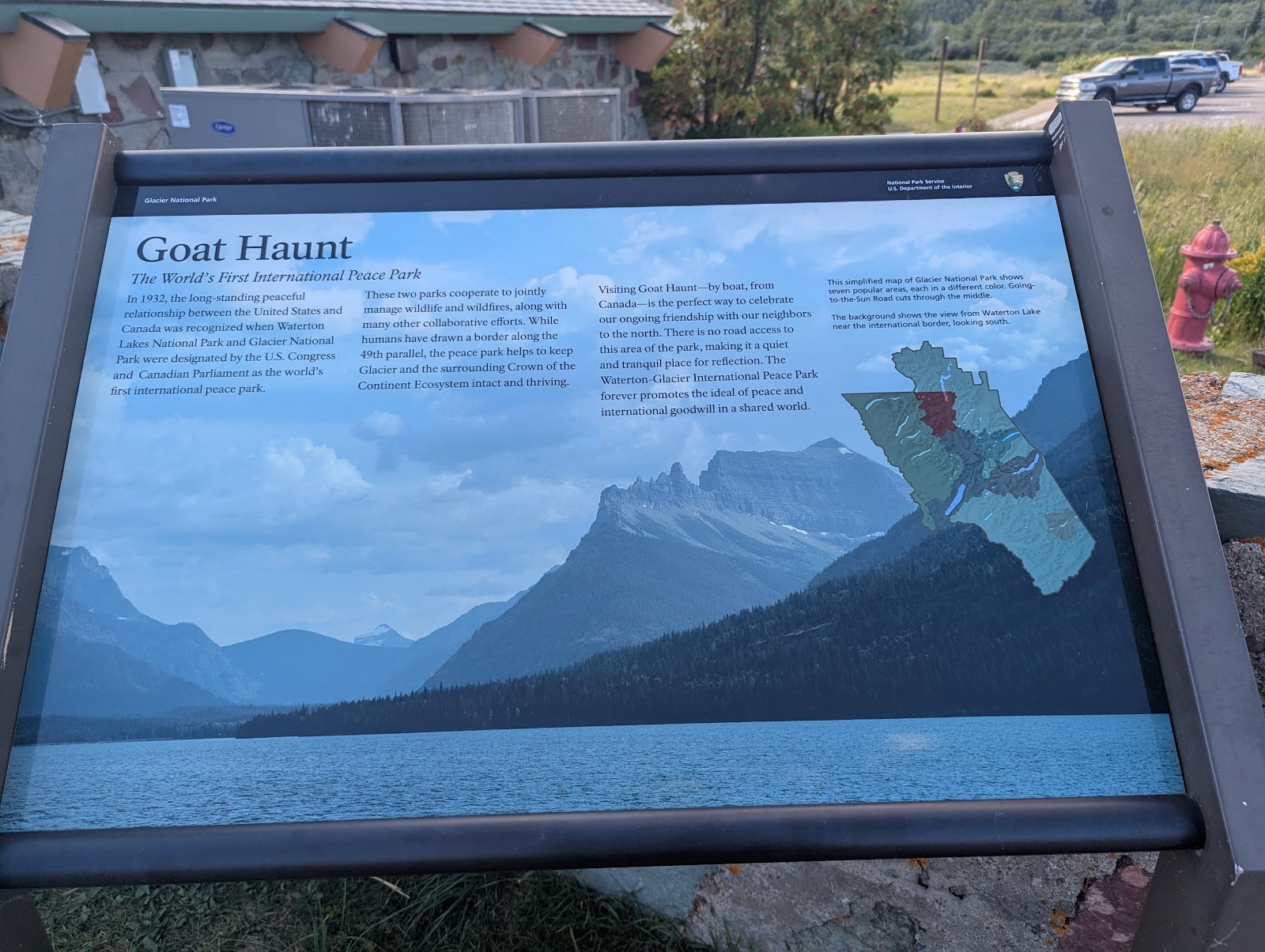 Informational sign at Glacier National Park showing Goat Haunt text, a mountain lake scene, and a map.