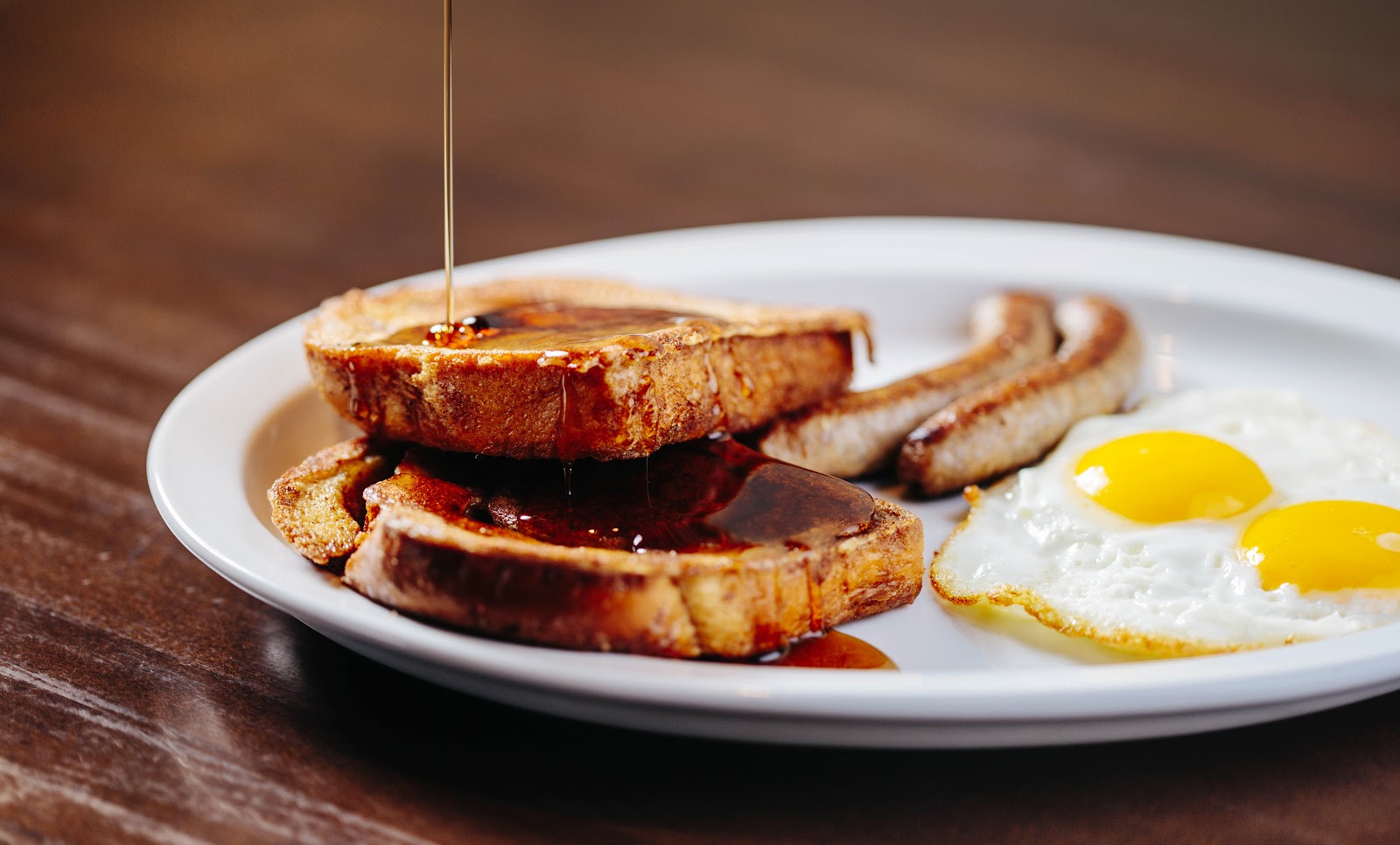 Breakfast plate at Glacier National Park featuring French toast with sausage and two sunny-side eggs, presented on a white plate.