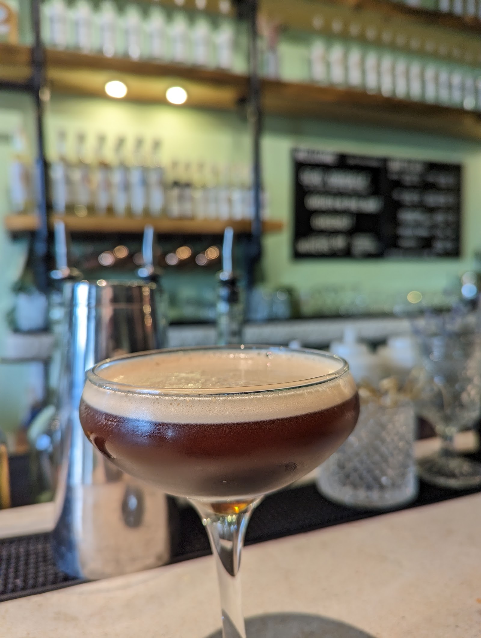 Elegant cocktail in a coupe glass sits at a Glacier National Park bar, with taps and soft lighting behind.