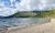 Pebble beach along a calm lake with forested mountains in Glacier National Park; hikers near the shore as clouds drift.