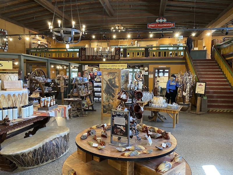 Inside a Yellowstone National Park gift shop with wooden tables, crafts, glass stones, and a staircase to the gallery.