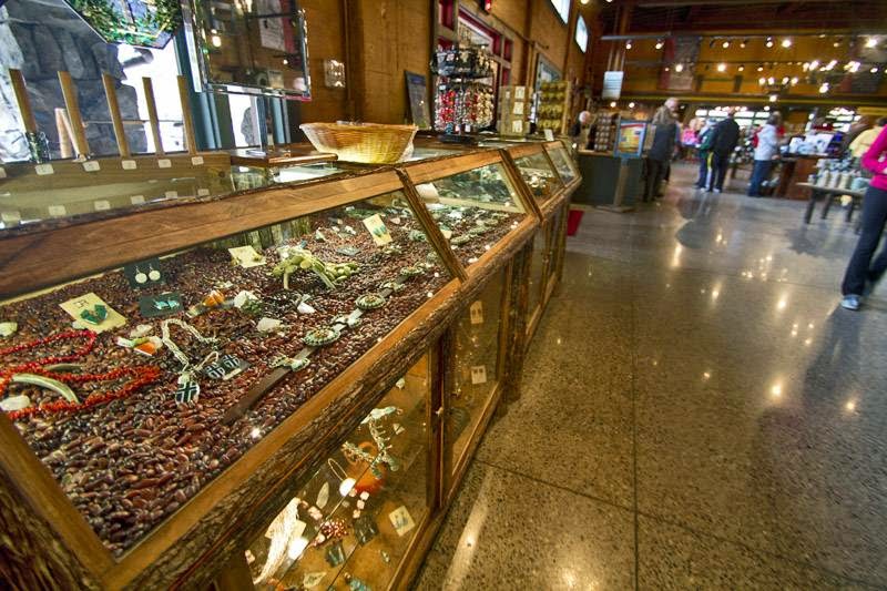 Inside a Yellowstone National Park gift shop, a long glass display case of bead jewelry and trinkets, with wooden shelves and shoppers nearby.