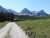 Gravel campground road in Glacier National Park winds toward evergreen forest and jagged, snow‑dusted mountains under a clear blue sky.