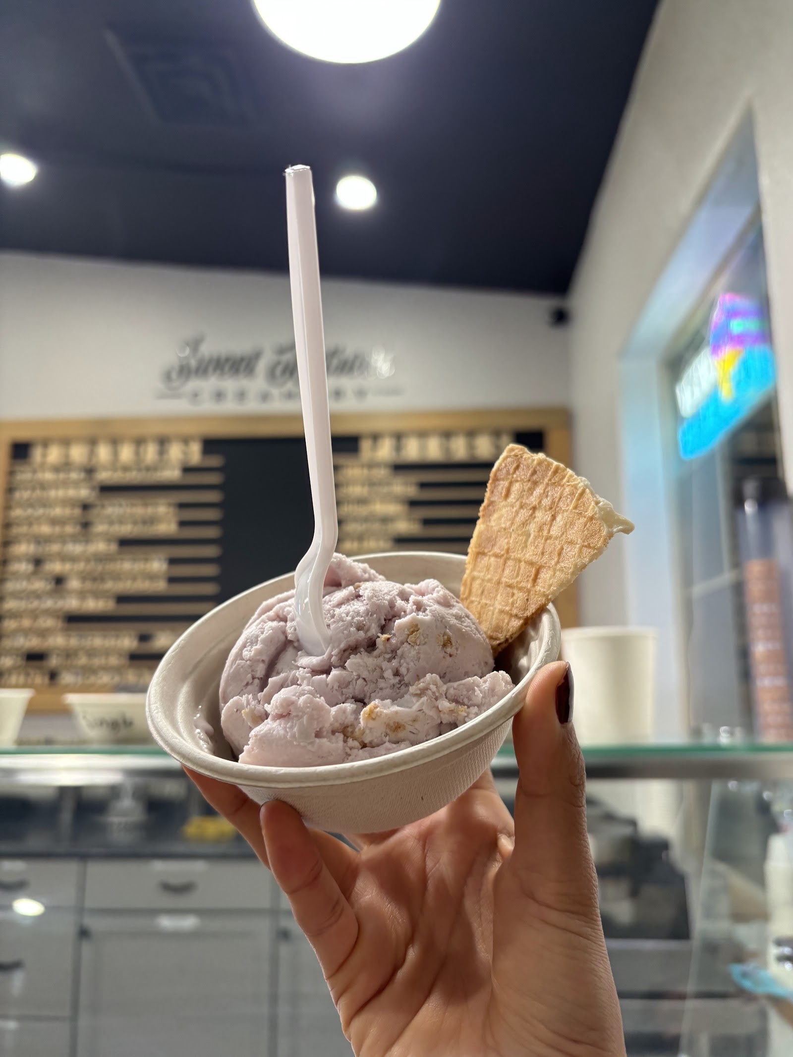 Lavender-hued ice cream scoop in a cup with a waffle cone piece at Sweet Retreat Creamery in Glacier National Park.