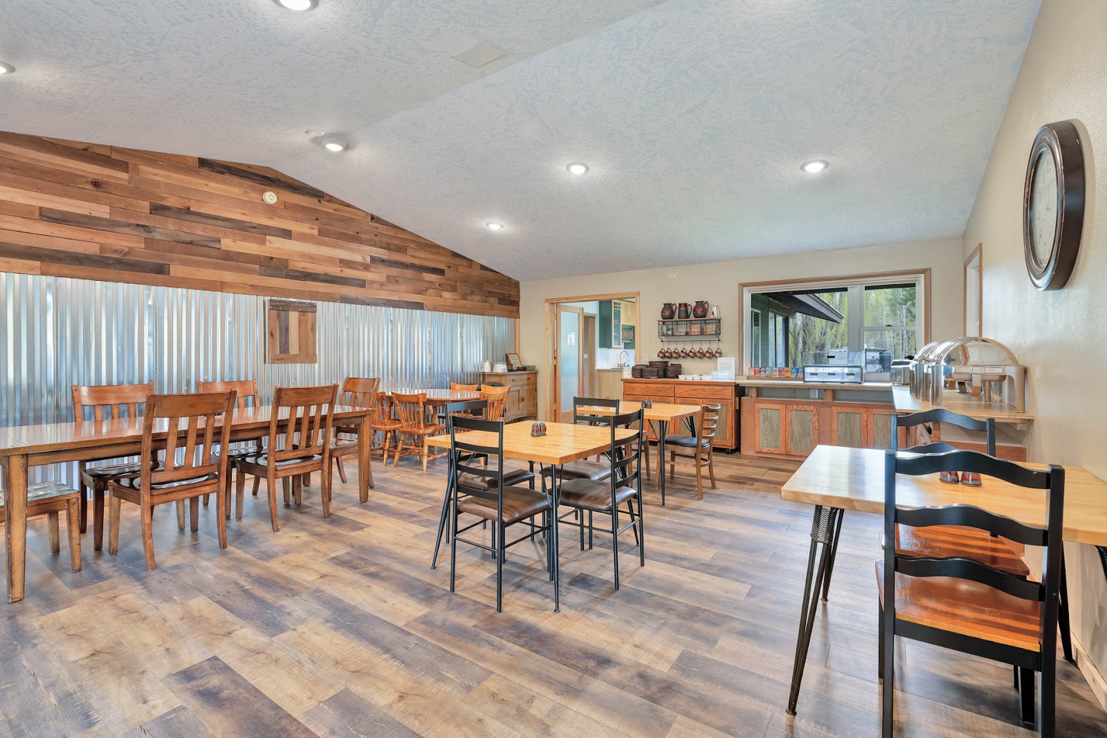 Rustic dining hall with wooden tables and chairs, a corrugated metal wall, and a breakfast counter in Glacier National Park.