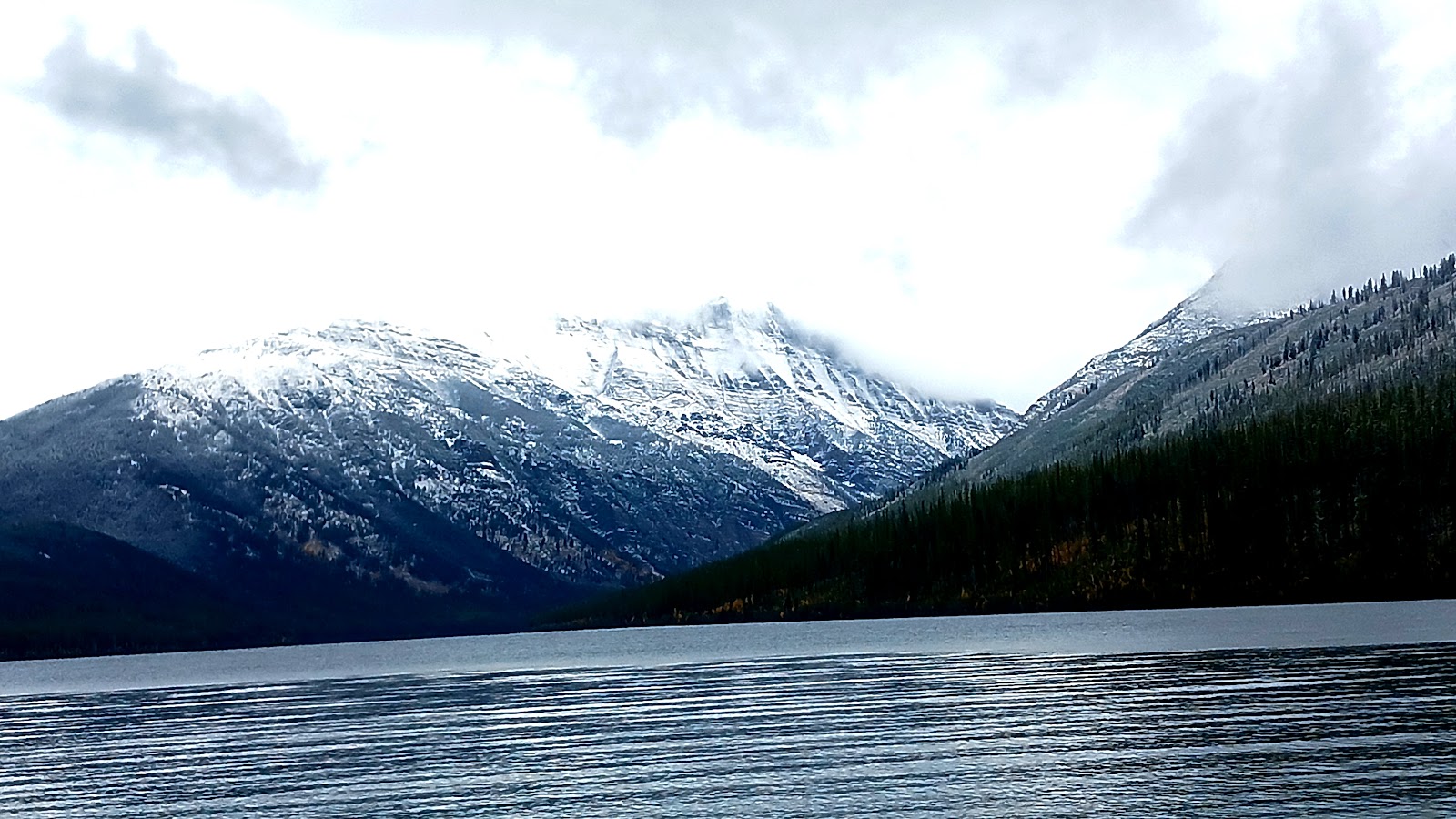 Long Knife Peak looms snowcapped above a dark forest and tranquil lake in Glacier National Park.
