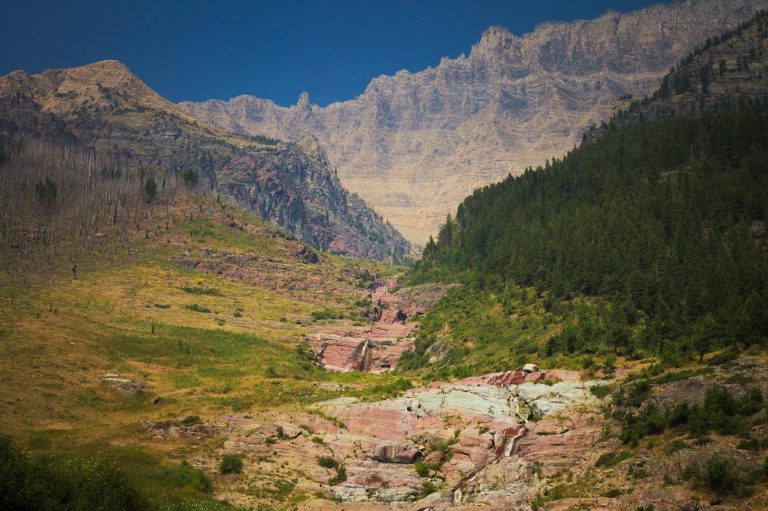 Long Knife Peak overlook in Glacier National Park frames a valley with red rock slopes and dense evergreen forests.