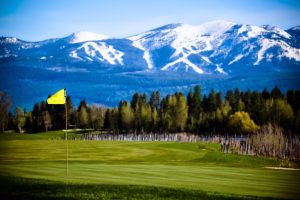 Yellow flag flutters on a pristine green with snow-capped peaks behind, in Glacier National Park.