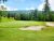 Whitefish Lake Golf Club green with sand bunkers and tall pines set against Glacier National Park scenery.