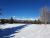 Snow-covered meadow near Whitefish Lake with distant Glacier National Park mountains beneath a clear blue sky.