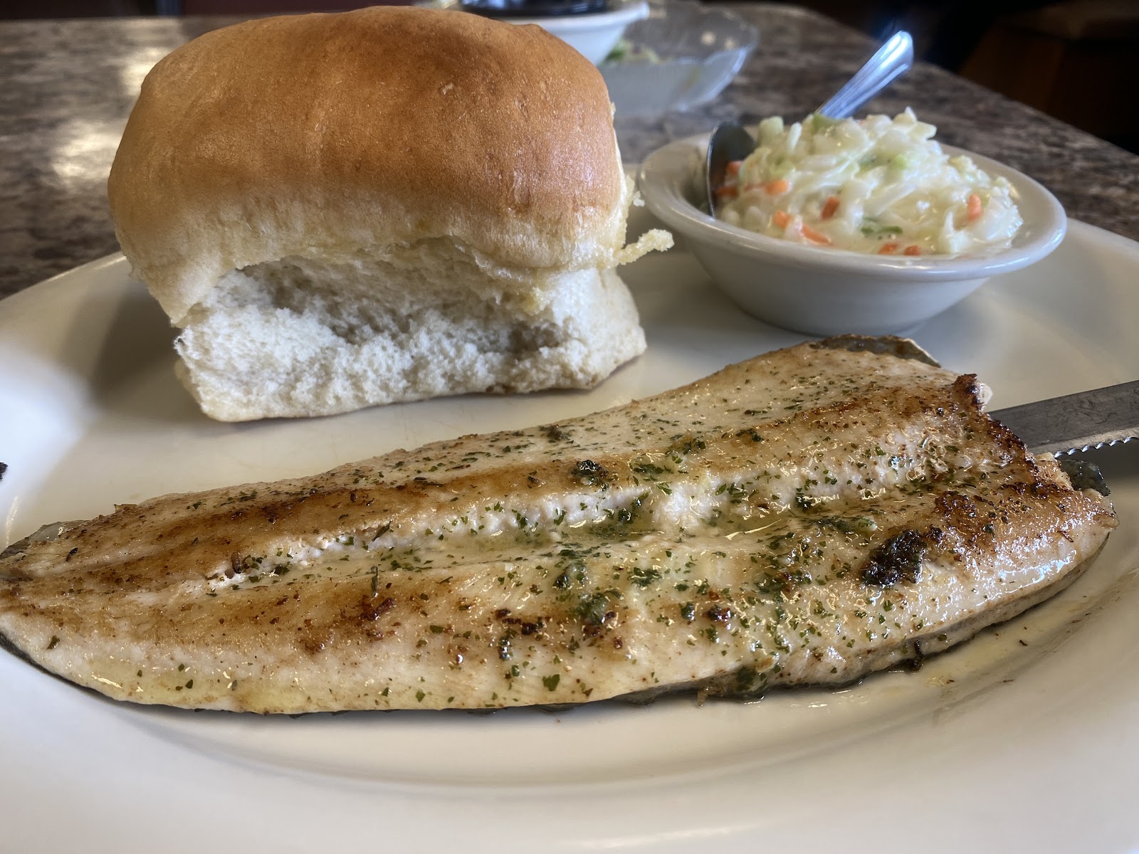 Grilled fish fillet with herbs, a soft roll, and a side of coleslaw at Piggyback Barbeque in Glacier National Park.