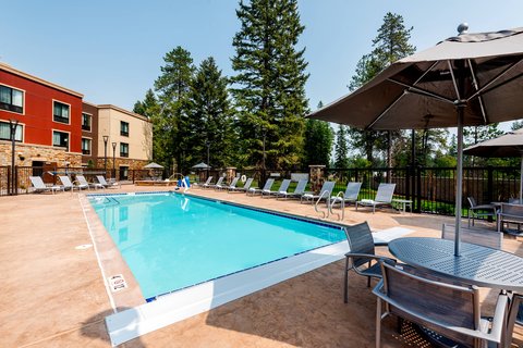 Outdoor pool area at TownePlace Suites by Marriott Whitefish Kalispell near Glacier National Park, with lounge chairs and umbrellas.