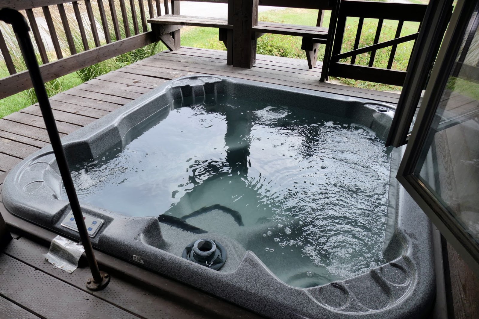 Hot tub on a wooden deck at Glacier National Park lodging area, surrounded by railing and green grass.