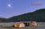 Glacier National Park campsite with lit tents and a central lodge under a moonlit sky at Bar W Guest Ranch campground.