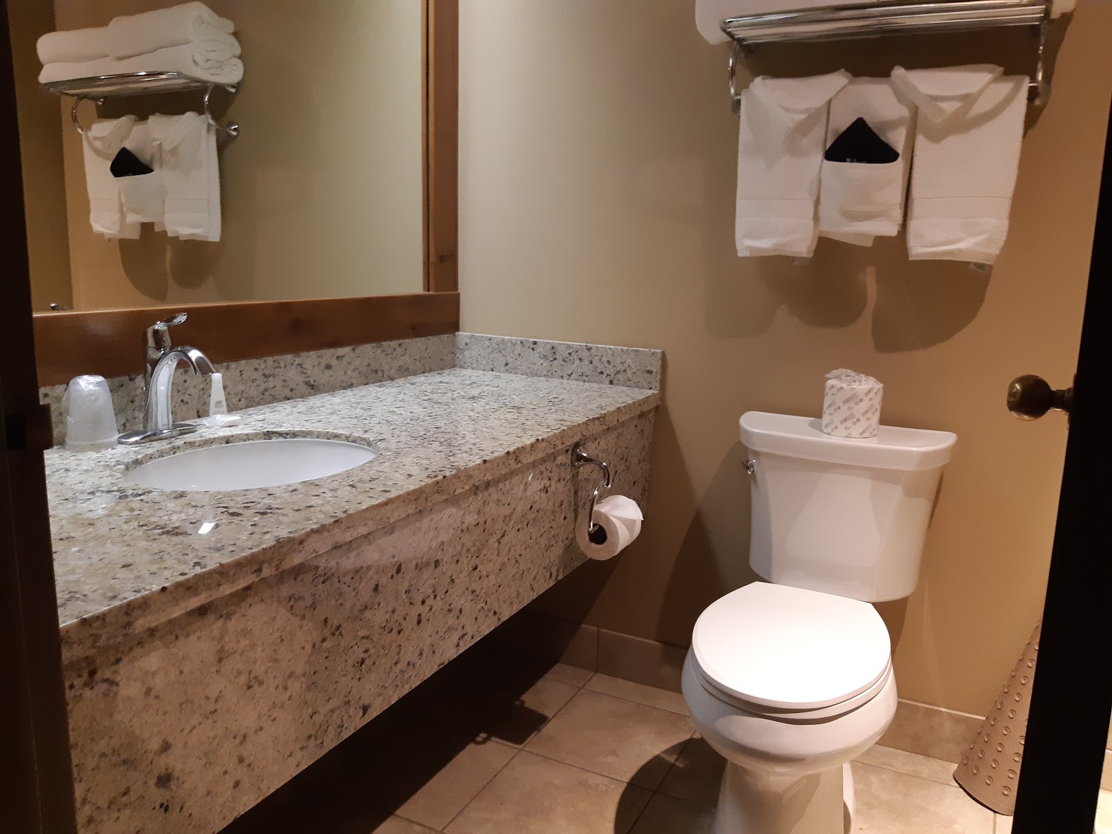 Contemporary lodge bathroom interior in Glacier National Park with granite countertop, sink, large mirror, and neatly folded towels.