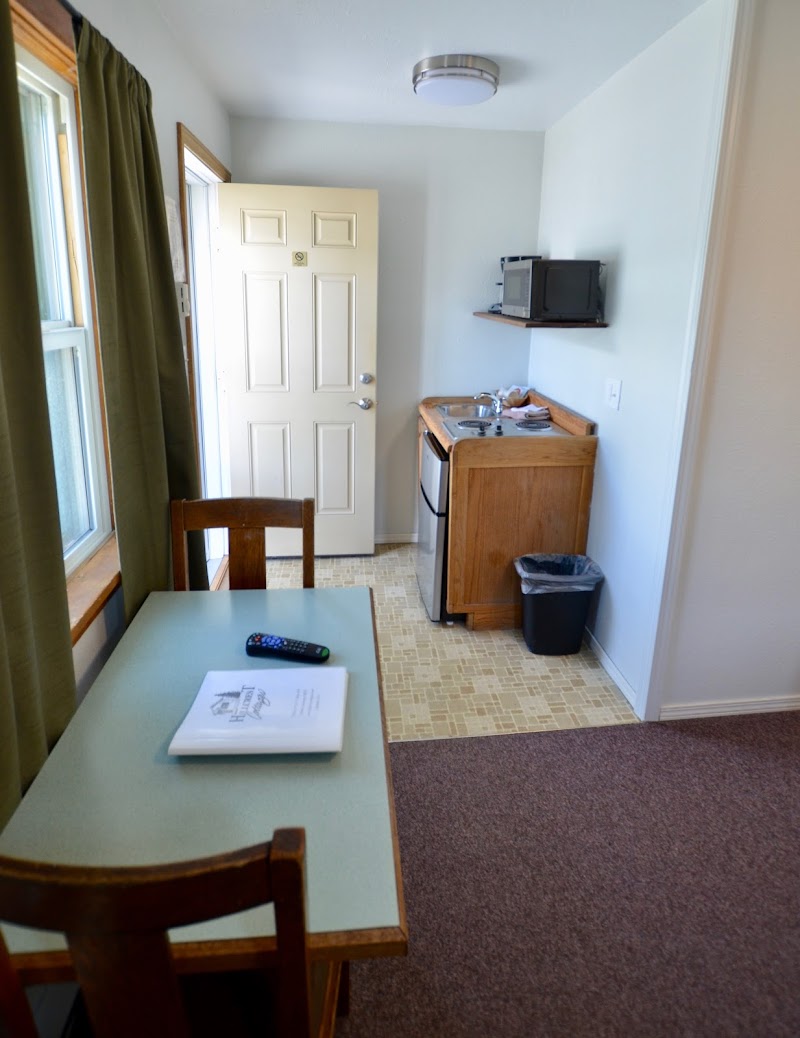 In Yellowstone National Park lodging, a kitchenette with sink, mini fridge, microwave, wooden table and chairs beside a window.