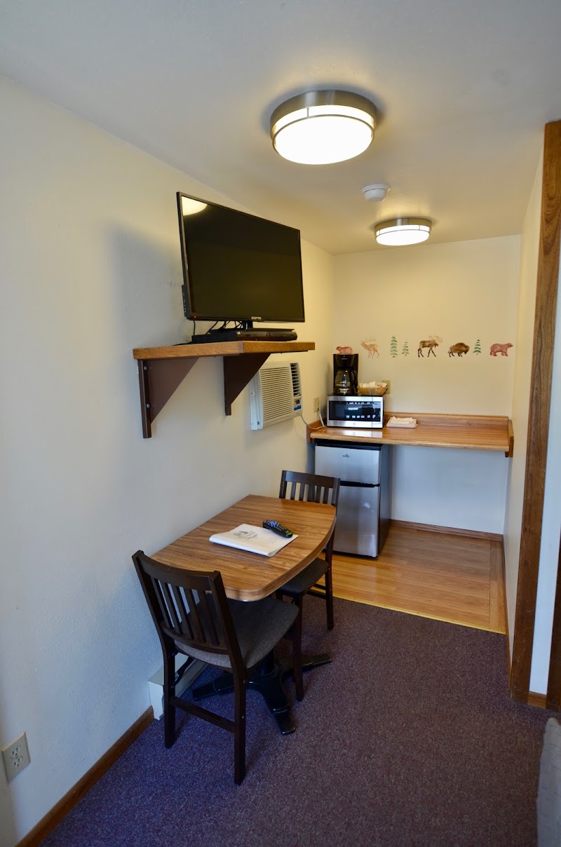 Cozy Yellowstone National Park lodging with wall-mounted TV, compact kitchenette, two-seat table, mini fridge, microwave, and animal decals.