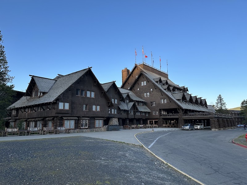 Dark wooden lodge with steep gabled roofs and many windows, flags atop near the entrance in Yellowstone National Park.