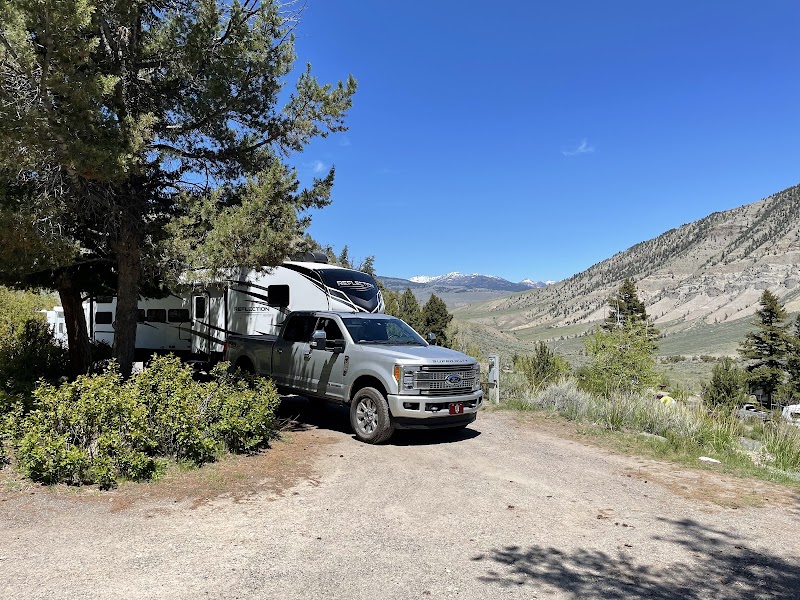 Silver pickup and large camper trailer parked among pines at a campground with distant mountains in Yellowstone National Park.